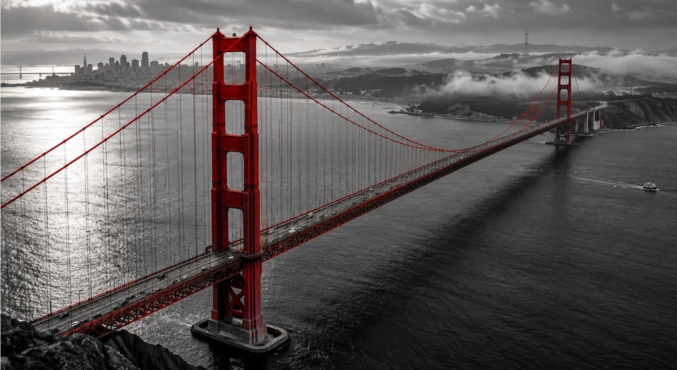 Golden Gate Bridge in black and white with its towers and cables in crimson, spanning the bay toward the city
